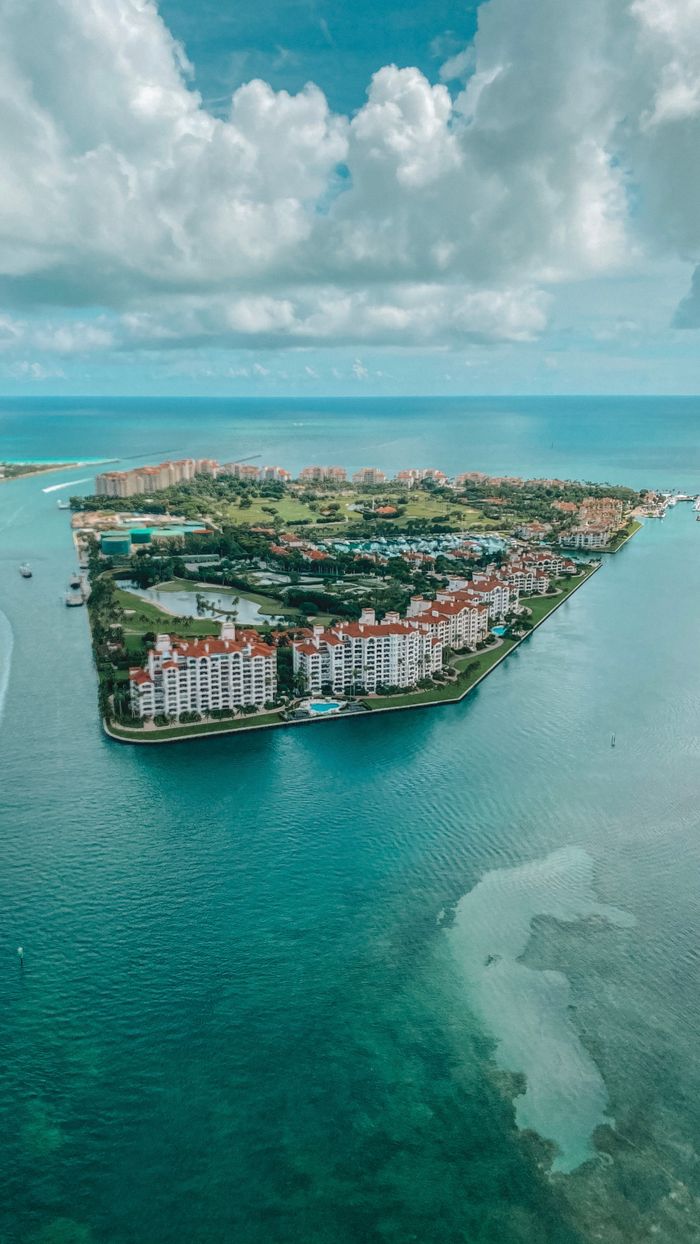 Stunning aerial photograph showcasing a coastal island with modern buildings and lush greenery surrounded by turquoise ocean waters.