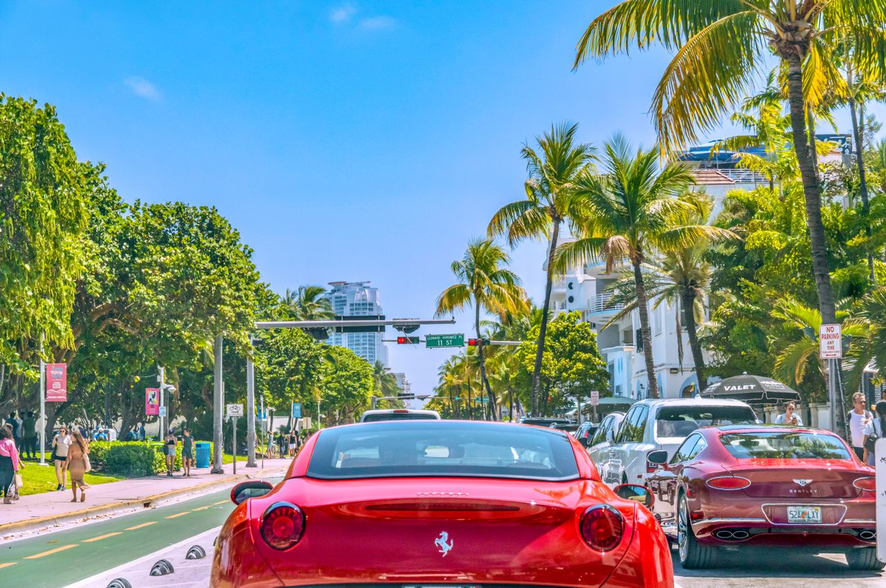 Colorful scene on Miami Beach's streets filled with luxury cars, palm trees, and bright sunlight.