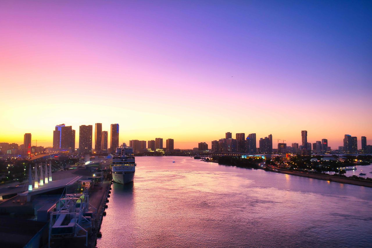 A stunning panoramic view of Miami's skyline at sunset, showcasing buildings, water, and a cruise ship.